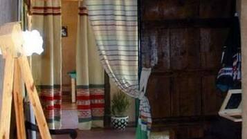 Une pièce rustique avec un plancher en bois, un chevalet en bois sur lequel est posée une toile vierge, un luminaire suspendu et un rideau à rayures.