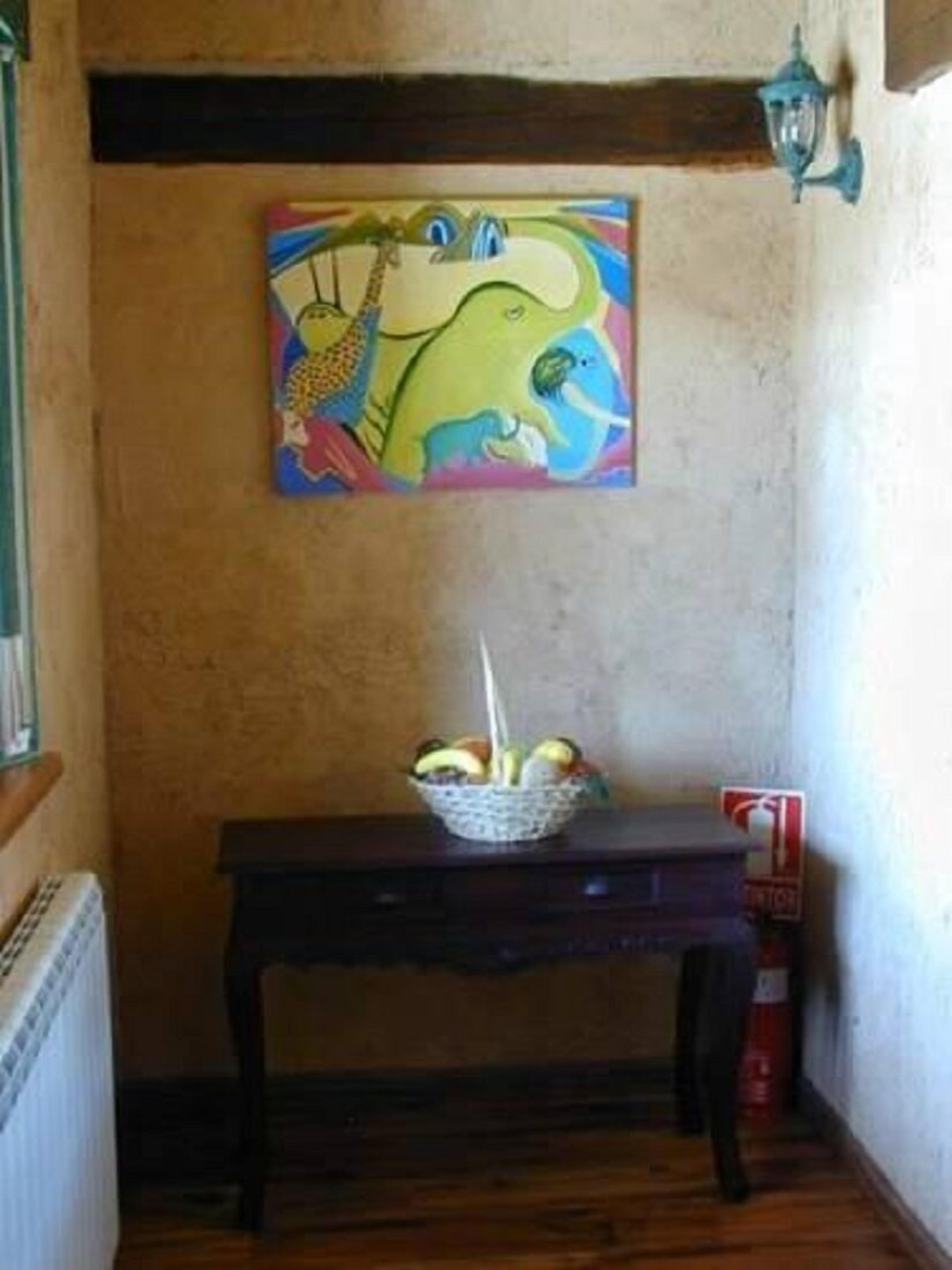 Quarto com pintura de girafa na parede, uma mesinha com uma fruteira e um extintor de incêndio no chão.