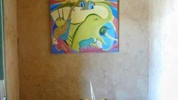 Quarto com pintura de girafa na parede, uma mesinha com uma fruteira e um extintor de incêndio no chão.