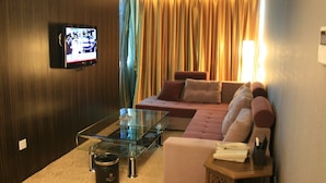 A modern living room with a glass coffee table, a sofa, and a television mounted on the wall. - Pengda Hotel Guangzhou (Guangzhou)