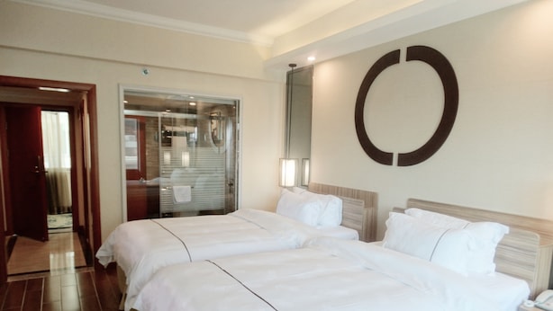 A hotel room with two beds, a large mirror, and a circular wall decoration. - Pengda Hotel Guangzhou (Guangzhou)