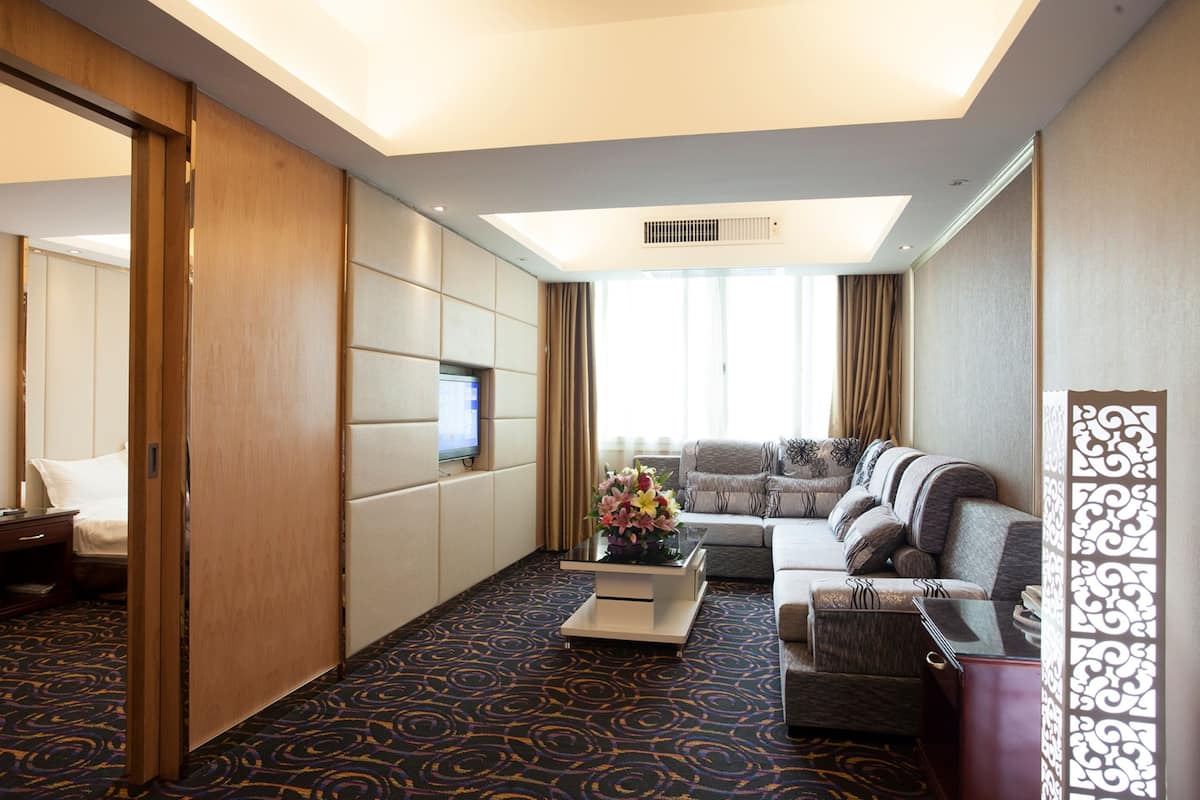 A hotel room with a sofa, a coffee table, a TV, and a decorative vase.