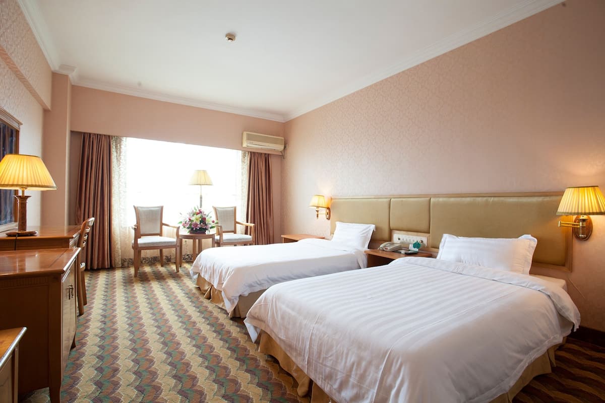 A hotel room with two beds, a desk, a chair, and a window with curtains.