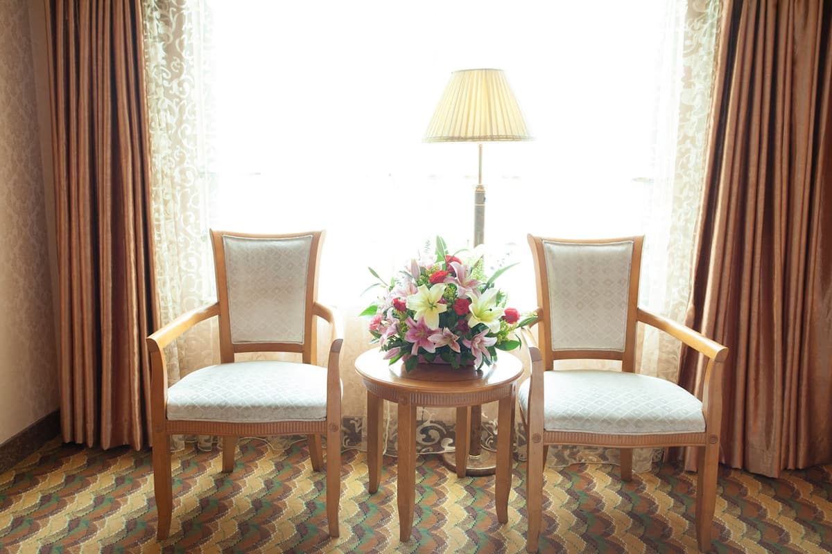 A room with two wooden chairs, a small round table with a floral arrangement, and a lamp.