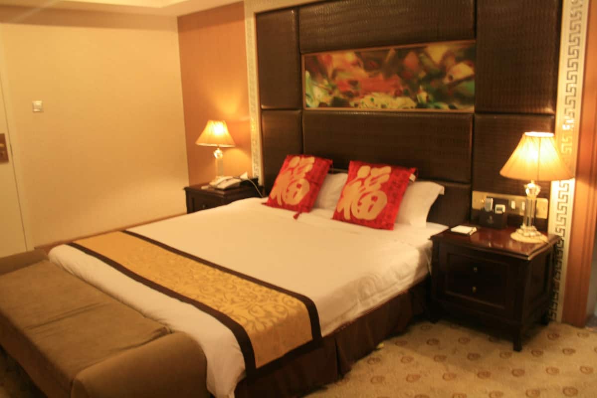 A hotel room with a large bed, two bedside tables with lamps, a headboard with a painting, and a patterned carpet.