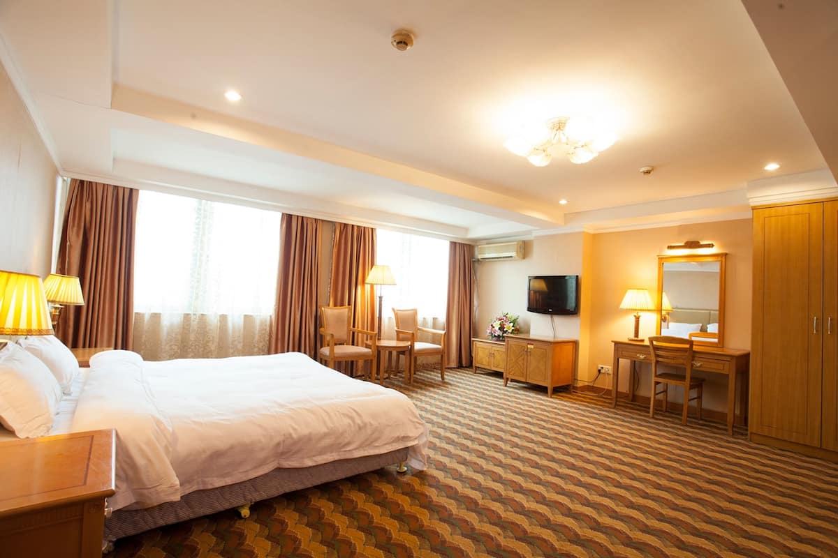 A hotel room with a large bed, a desk, a chair, a dresser, and a television.