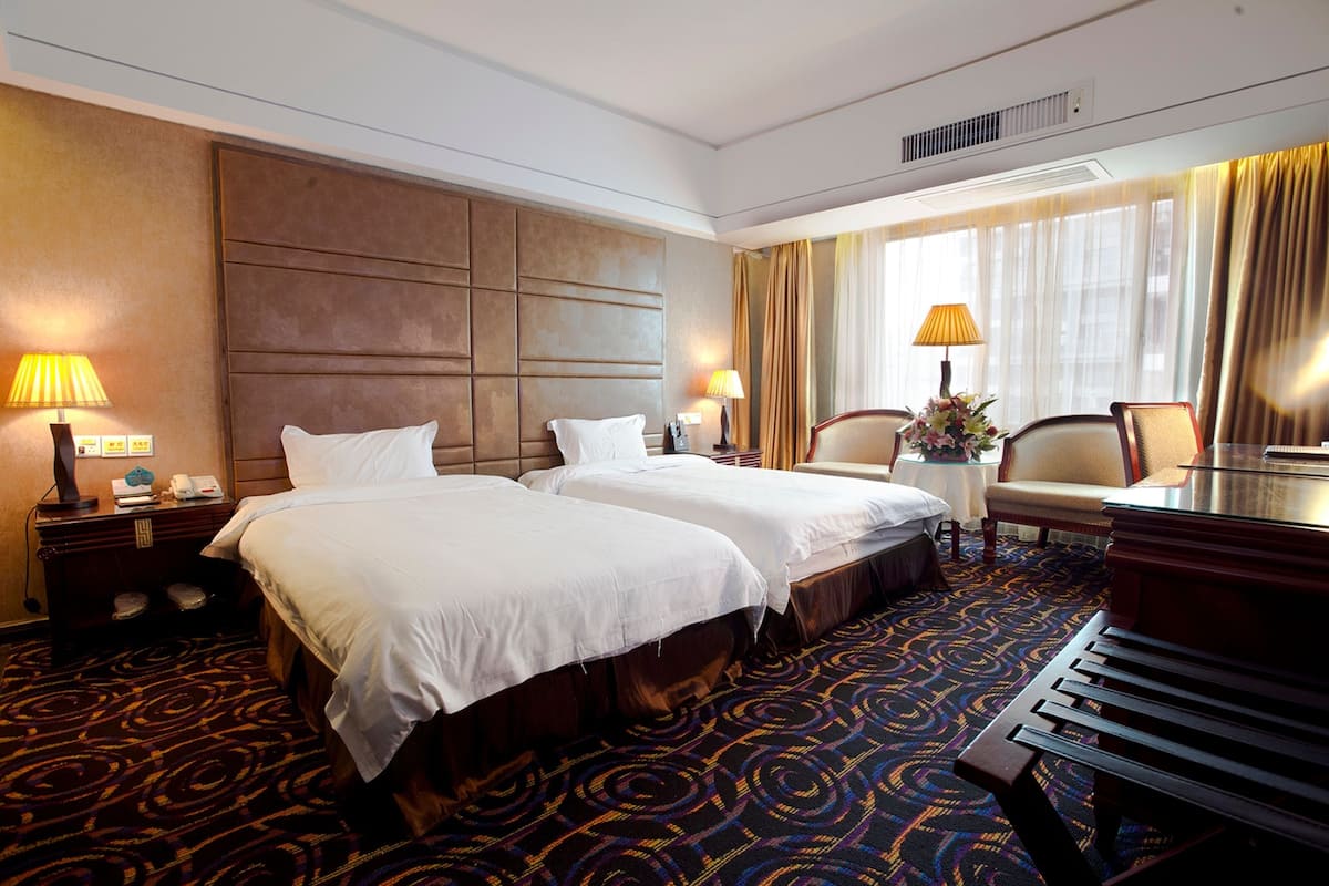 A hotel room with two beds, a desk, a chair, and a piano.