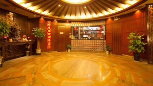 A lobby with a circular patterned floor, wooden paneling, a reception desk, and potted plants. - Pengda Hotel Guangzhou (Guangzhou)