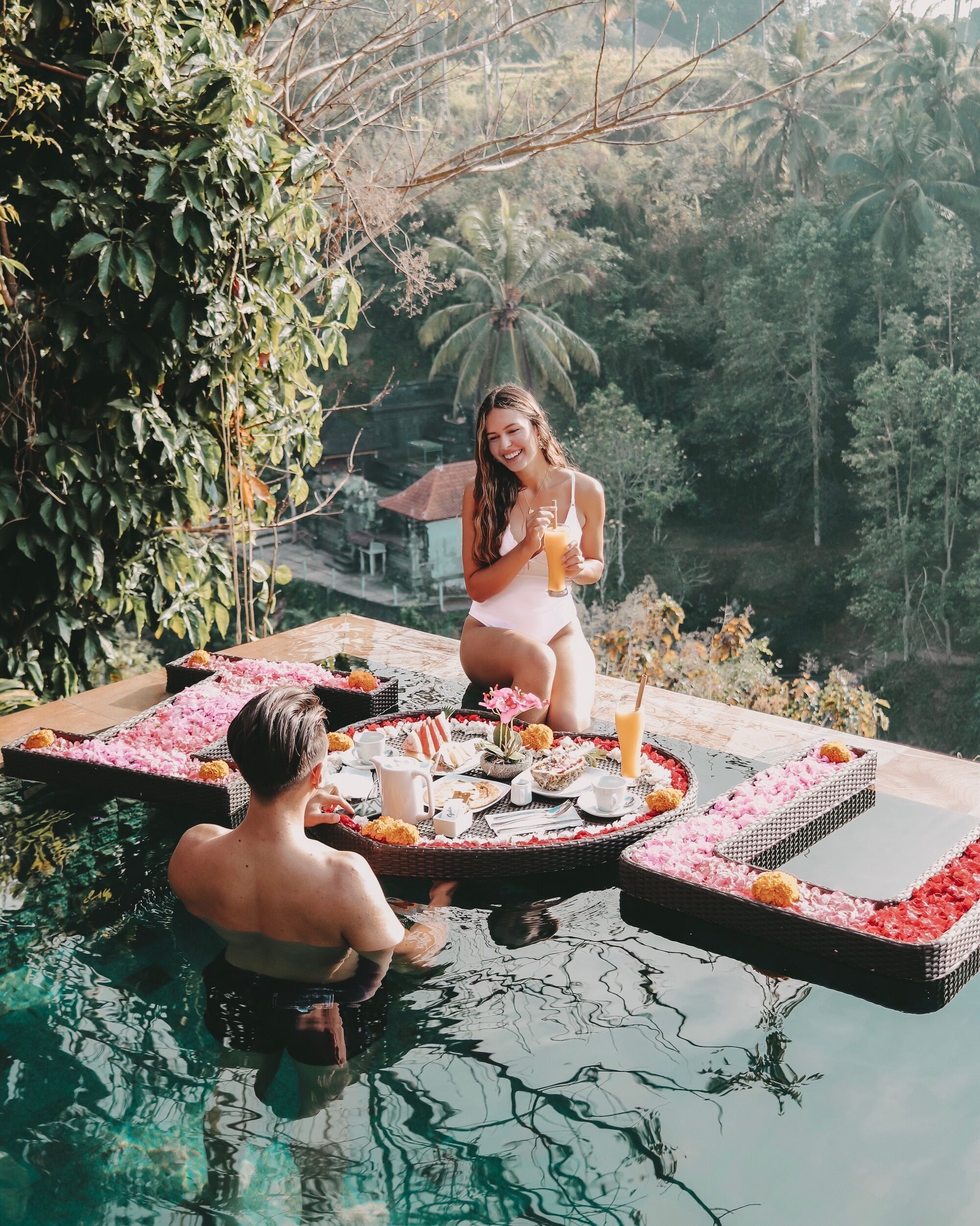 A couple enjoying a meal by a pool with tropical surroundings.