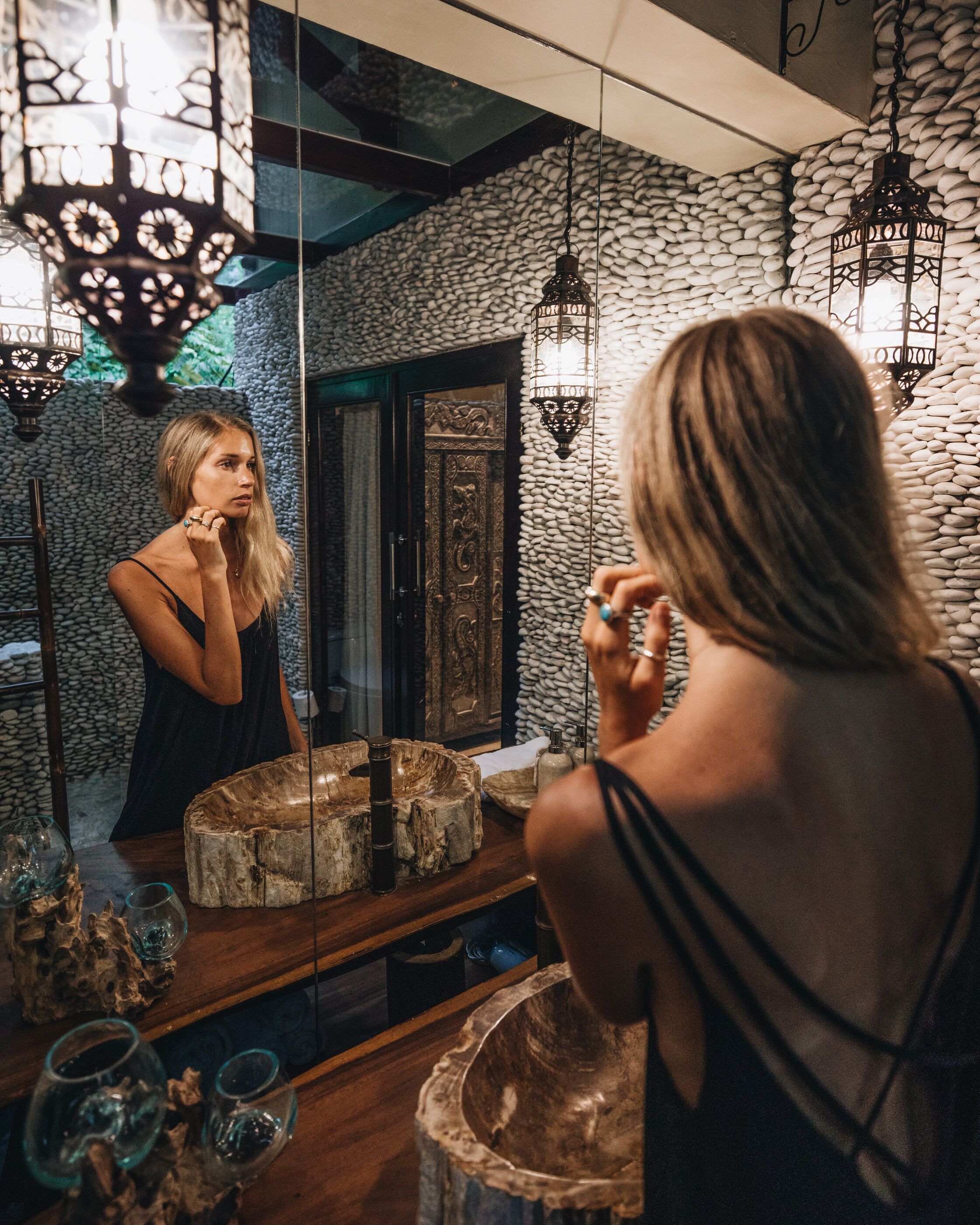 A bathroom with a large mirror, wooden vanity, and decorative stone wall.