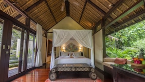 A four-poster bed with a canopy, a red patterned rug, and a view of lush greenery outside. - Villa Cella Bella (Ubud)