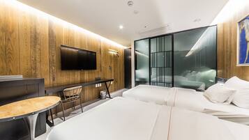 A modern hotel room with a wooden wall, a flat-screen TV, a desk with a chair, and two beds with white bedding.