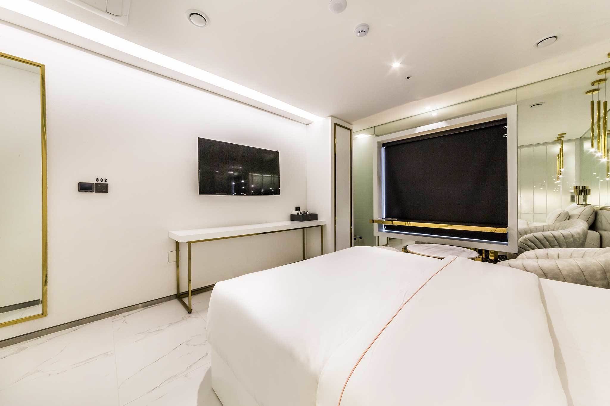 A modern hotel room with a large bed, a desk, a television, and a large mirror.