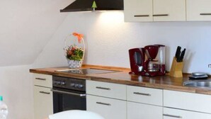 Une cuisine avec des meubles blancs, un plan de travail en bois, une machine à café et un bloc à couteaux.