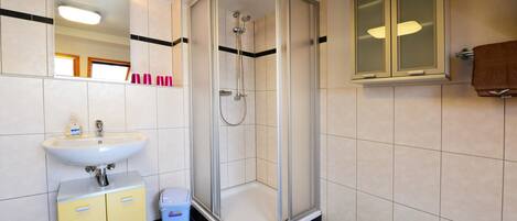 Une salle de bain moderne avec une douche à parois de verre, un lavabo avec un miroir au-dessus et un meuble avec une poubelle.