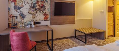 A hotel room with a bed, a desk with a chair, a TV mounted on the wall, and a wooden cabinet.