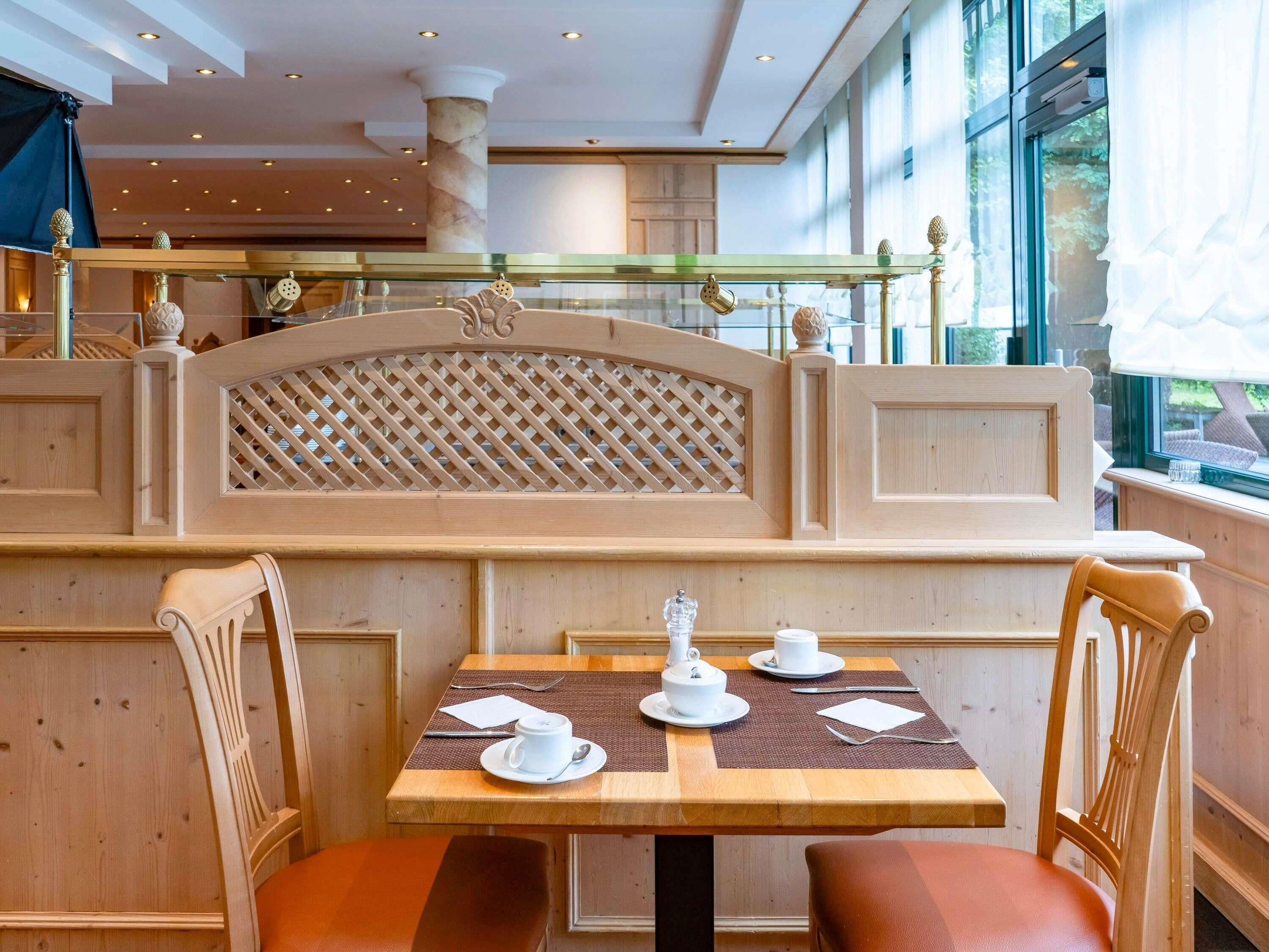 A wooden booth with a lattice partition, a table with white cups and saucers, and chairs.