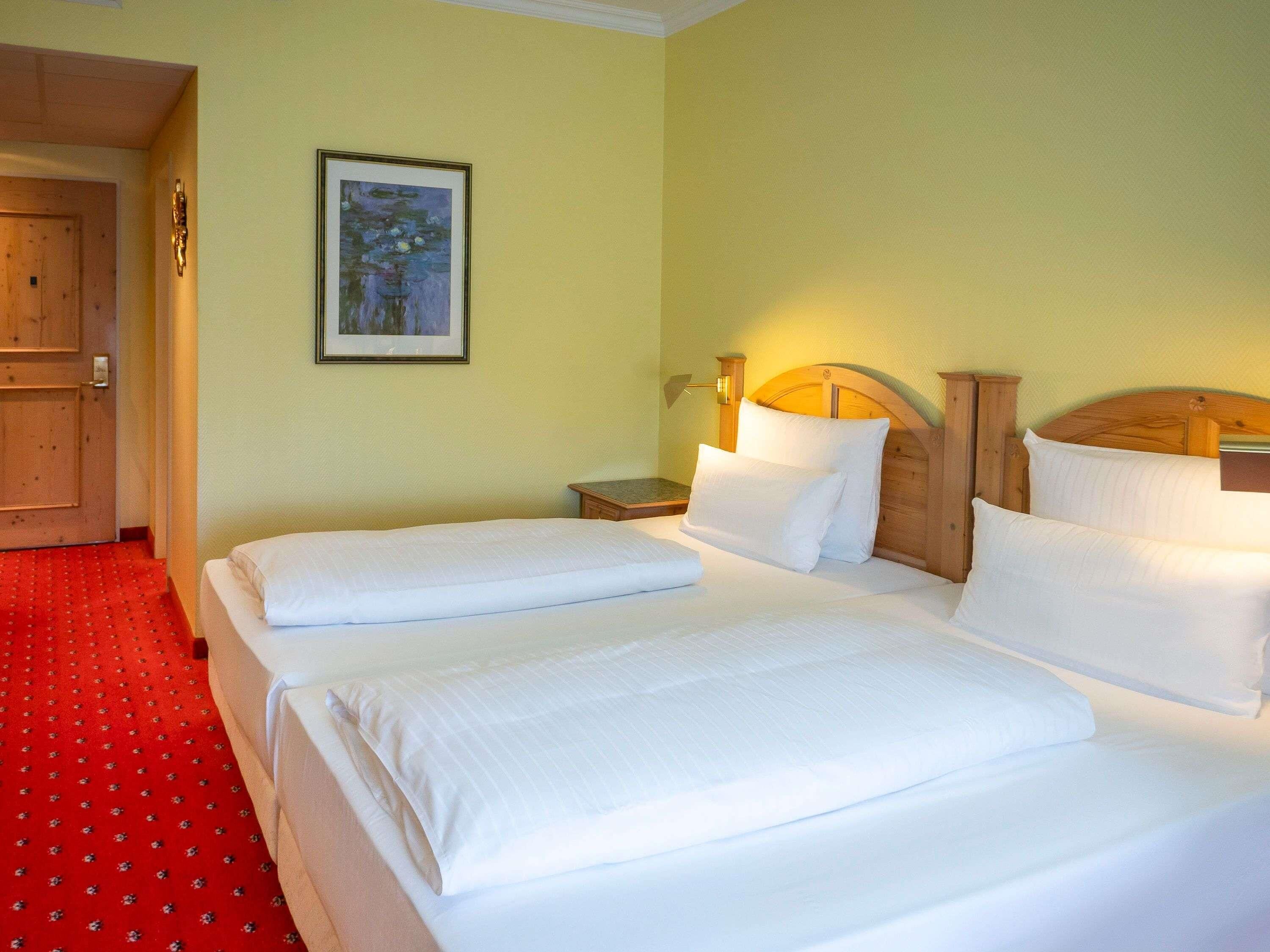 Una camera d'albergo con due letti, una testiera in legno, un comodino, un quadro incorniciato appeso al muro e un pavimento con tappeto rosso.