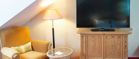 A hotel room with a sofa, a small round table, a TV on a wooden cabinet, and a lamp.
