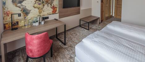 A hotel room with a bed, a desk with a chair, a map on the wall, and a TV.