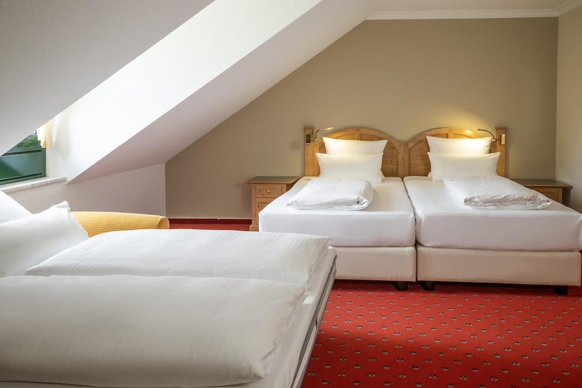 Une chambre d’hôtel avec deux lits, une moquette rouge à motifs et un plafond en pente.