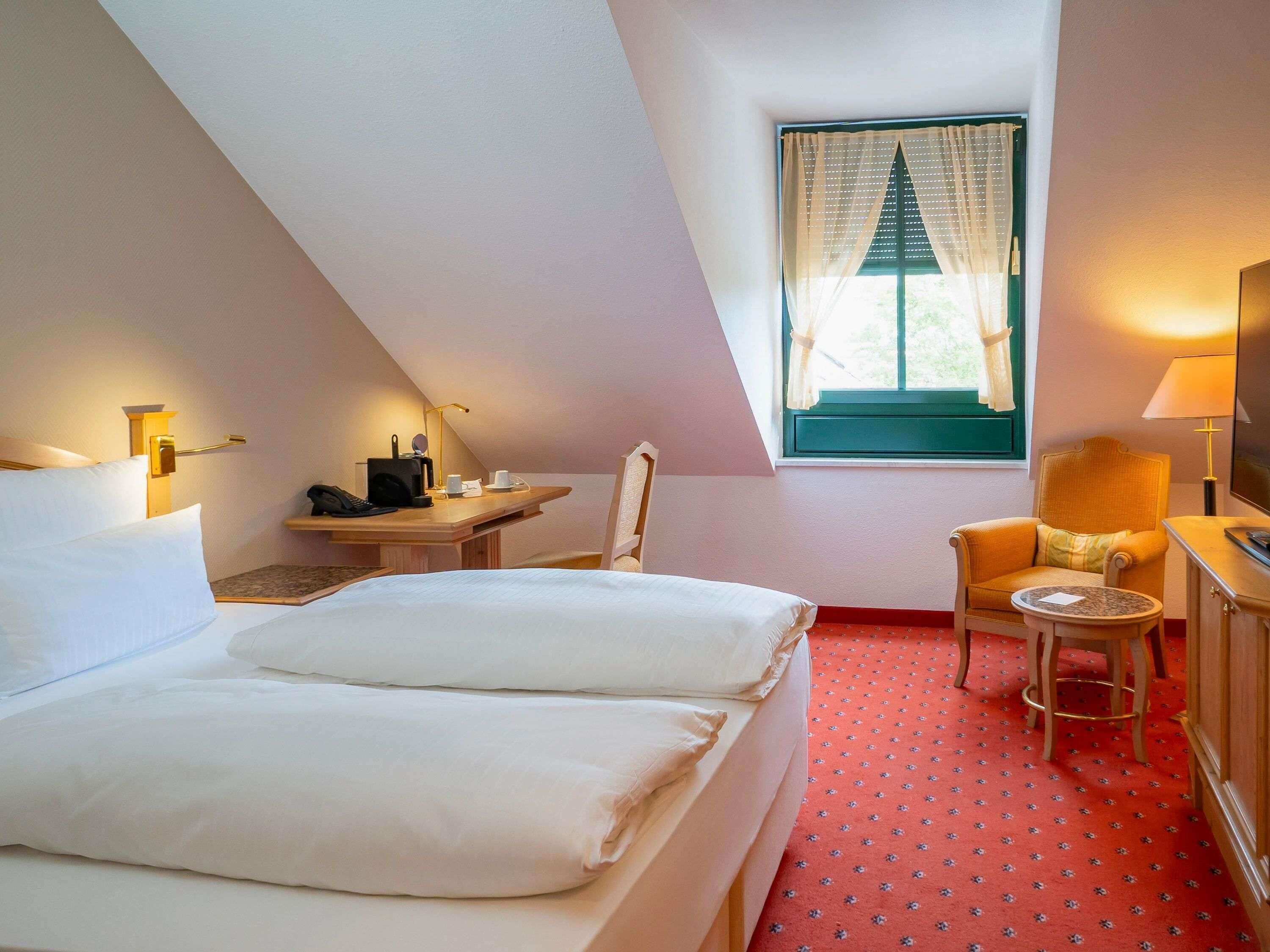 Hotelkamer met een bed, bureau, stoel, kleine tafel en raam met gordijnen.