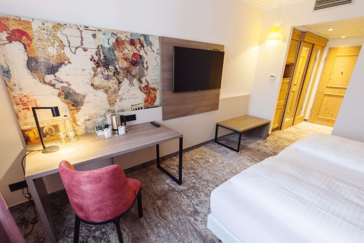 Une chambre d’hôtel avec un lit, un bureau et une chaise, une carte accrochée au mur, une télévision et une petite table.