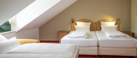 Habitación de hotel con dos camas, alfombra roja y techo inclinado.