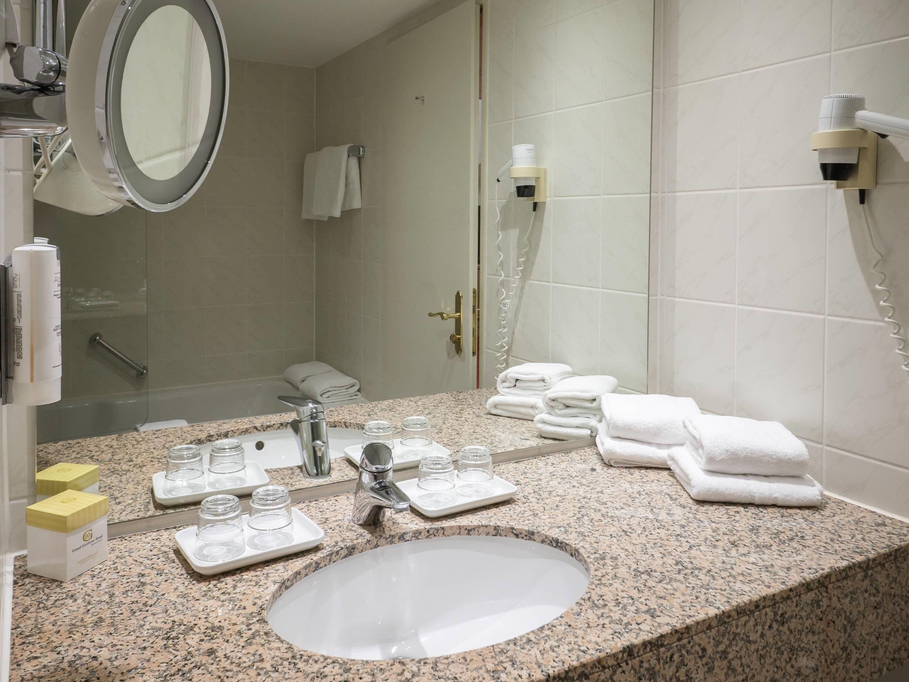 A bathroom with a granite countertop, a sink, a mirror, a towel rack, a shower, and a hairdryer.