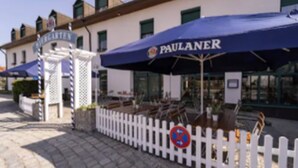 Ein Gebäude mit weißem Zaun und einem blauen Sonnenschirm mit der Aufschrift "PAULANER".