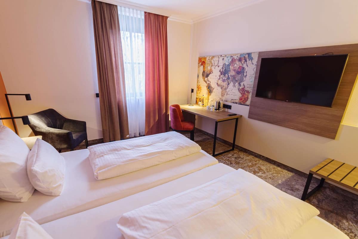 Ein Hotelzimmer mit zwei Betten, einem Schreibtisch, einem Stuhl, einem Fernseher und einer Karte an der Wand.