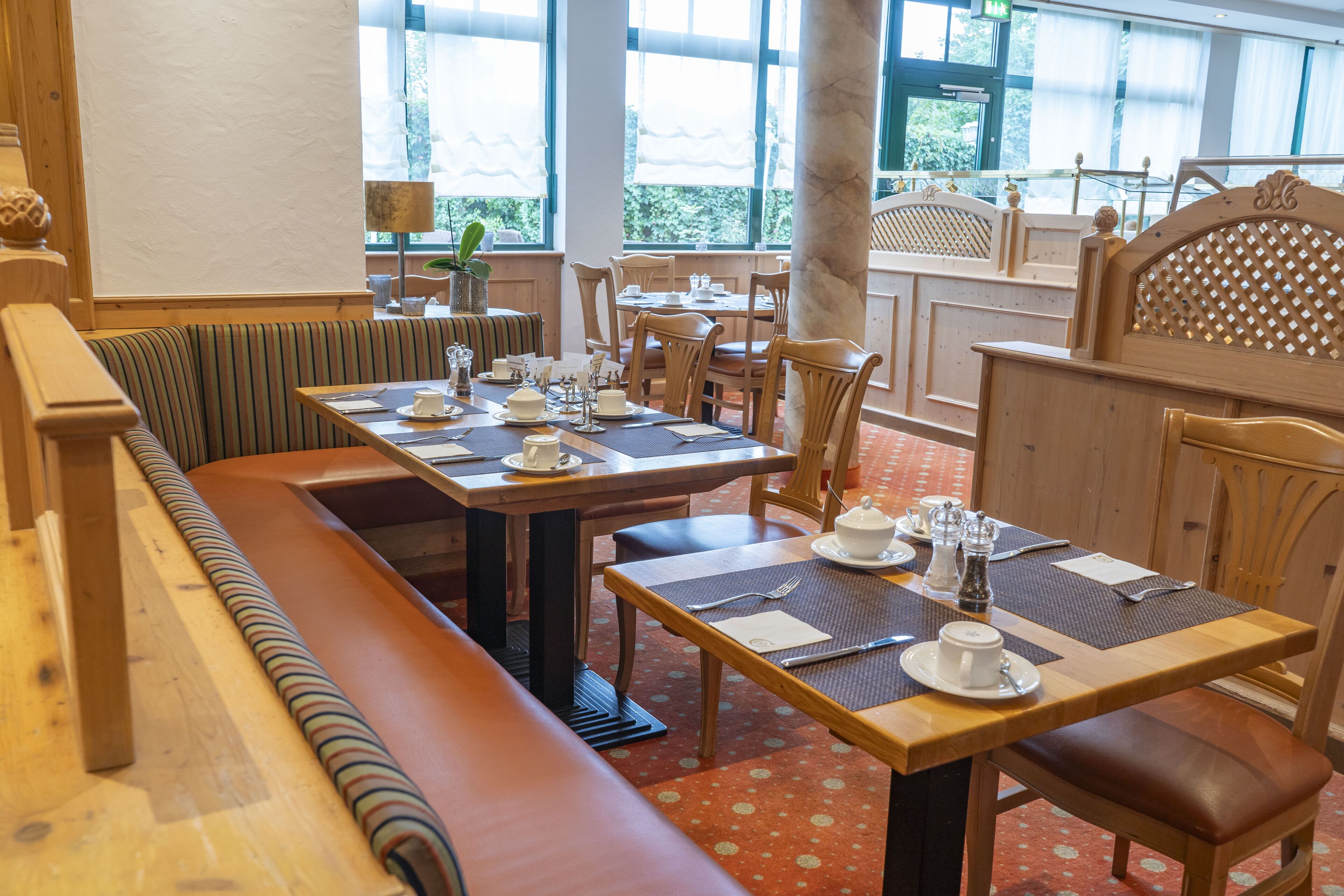 Een restaurant met houten meubels, zoals tafels en banken, en grote ramen met uitzicht op de omgeving.