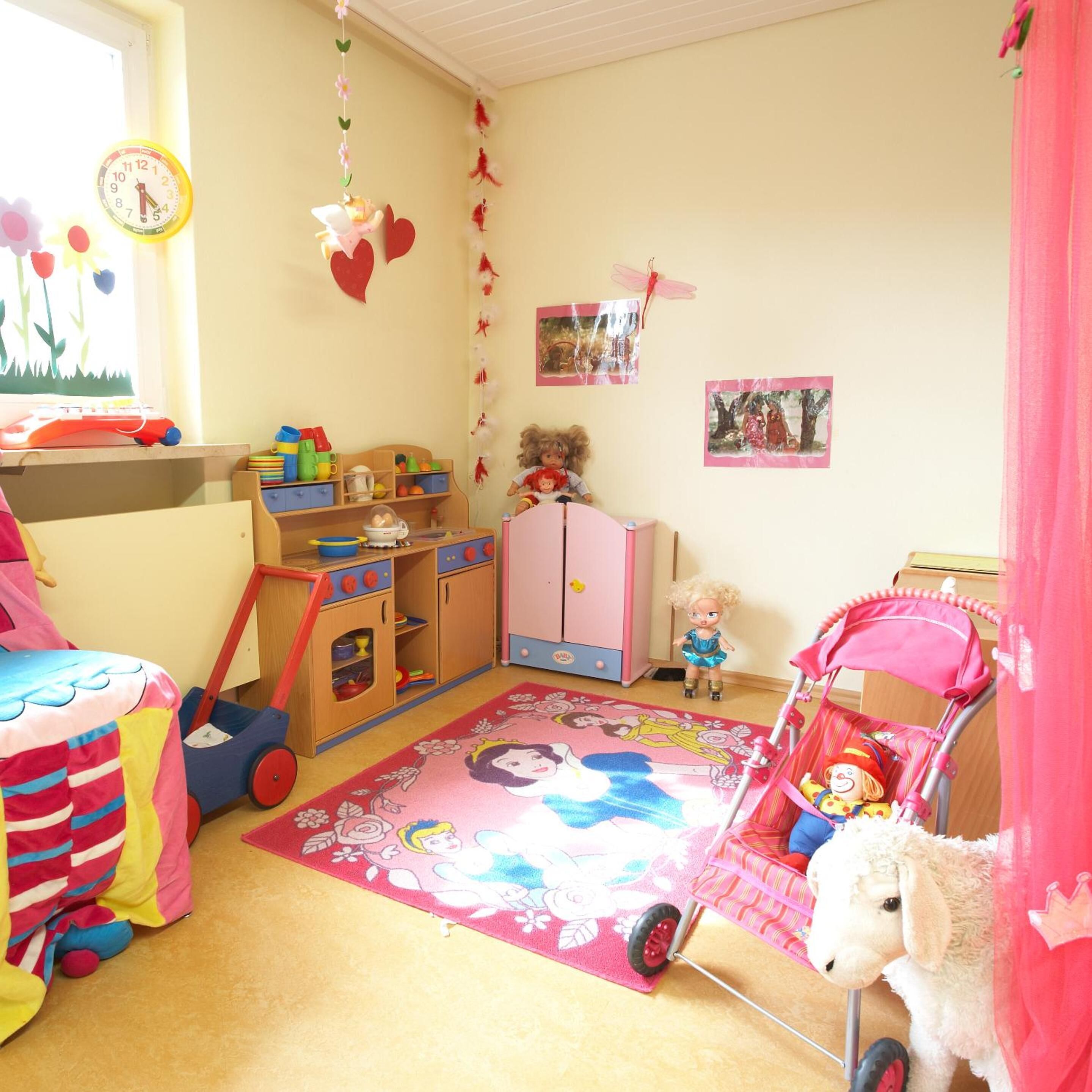 A child's playroom with a bed, a toy car, a pink stroller, and a bookshelf.
