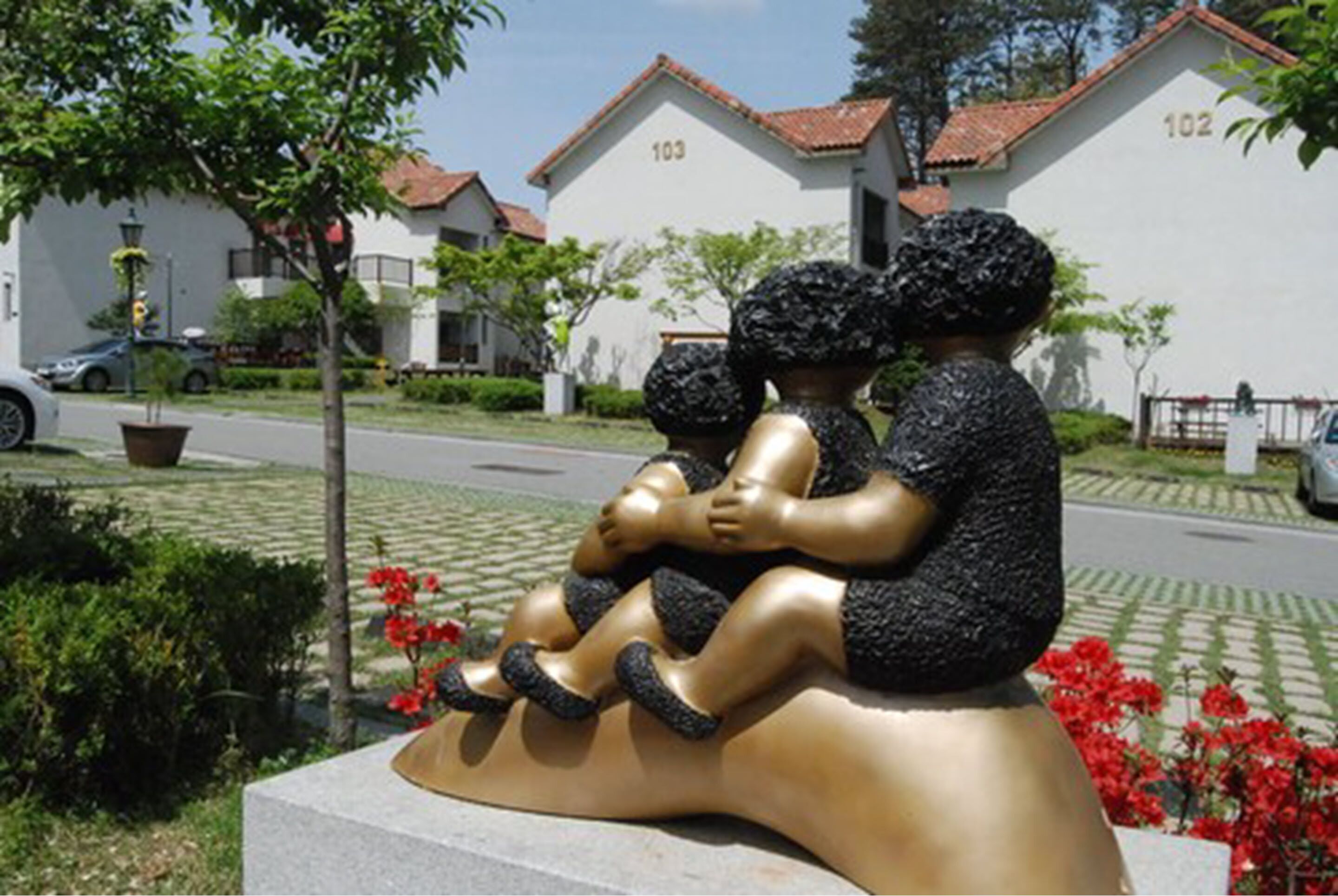 Una escultura de tres figuras en un jardín, con edificios al fondo.