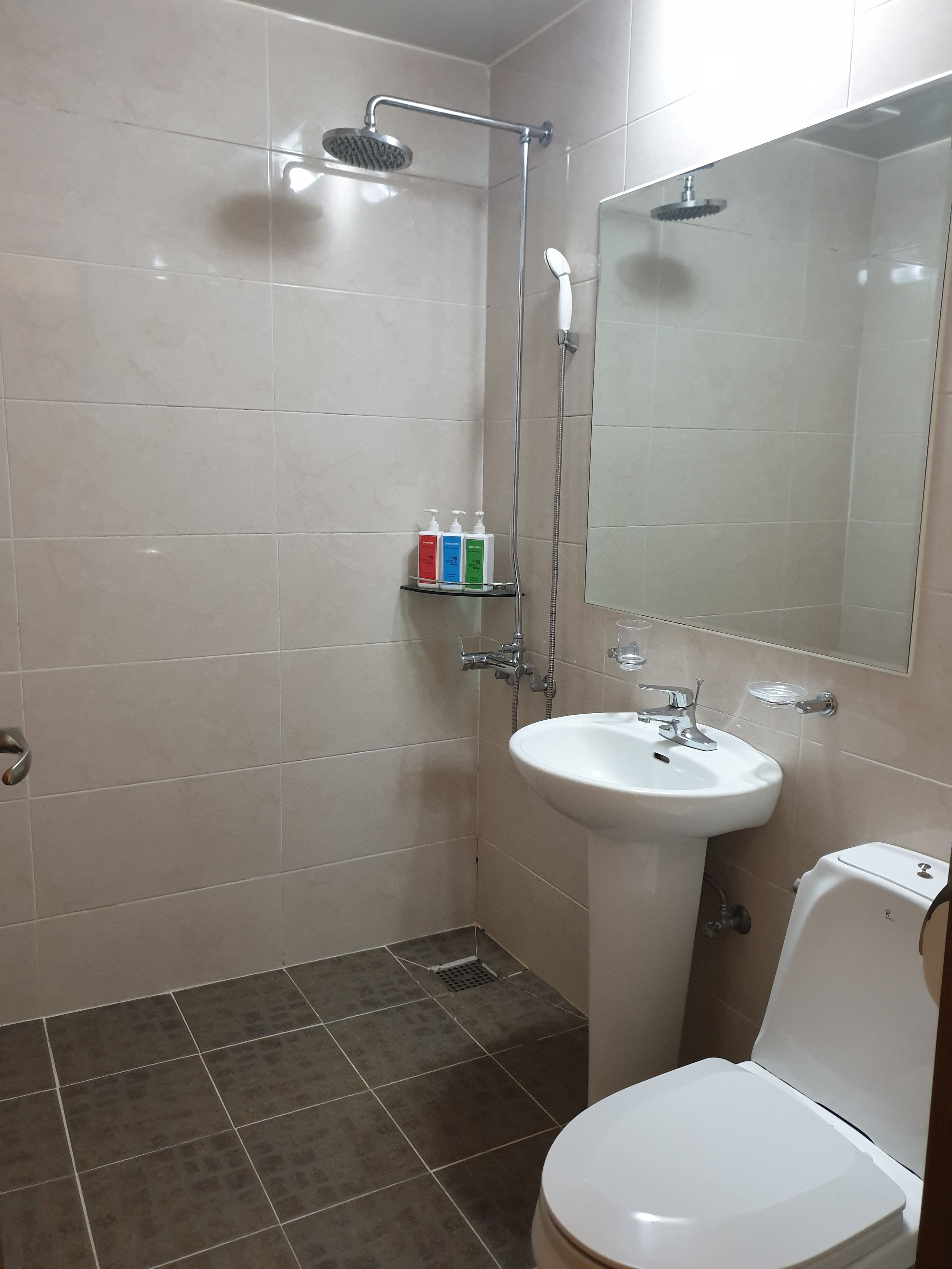 A bathroom with a shower, sink, toilet, and a shelf with toiletries.