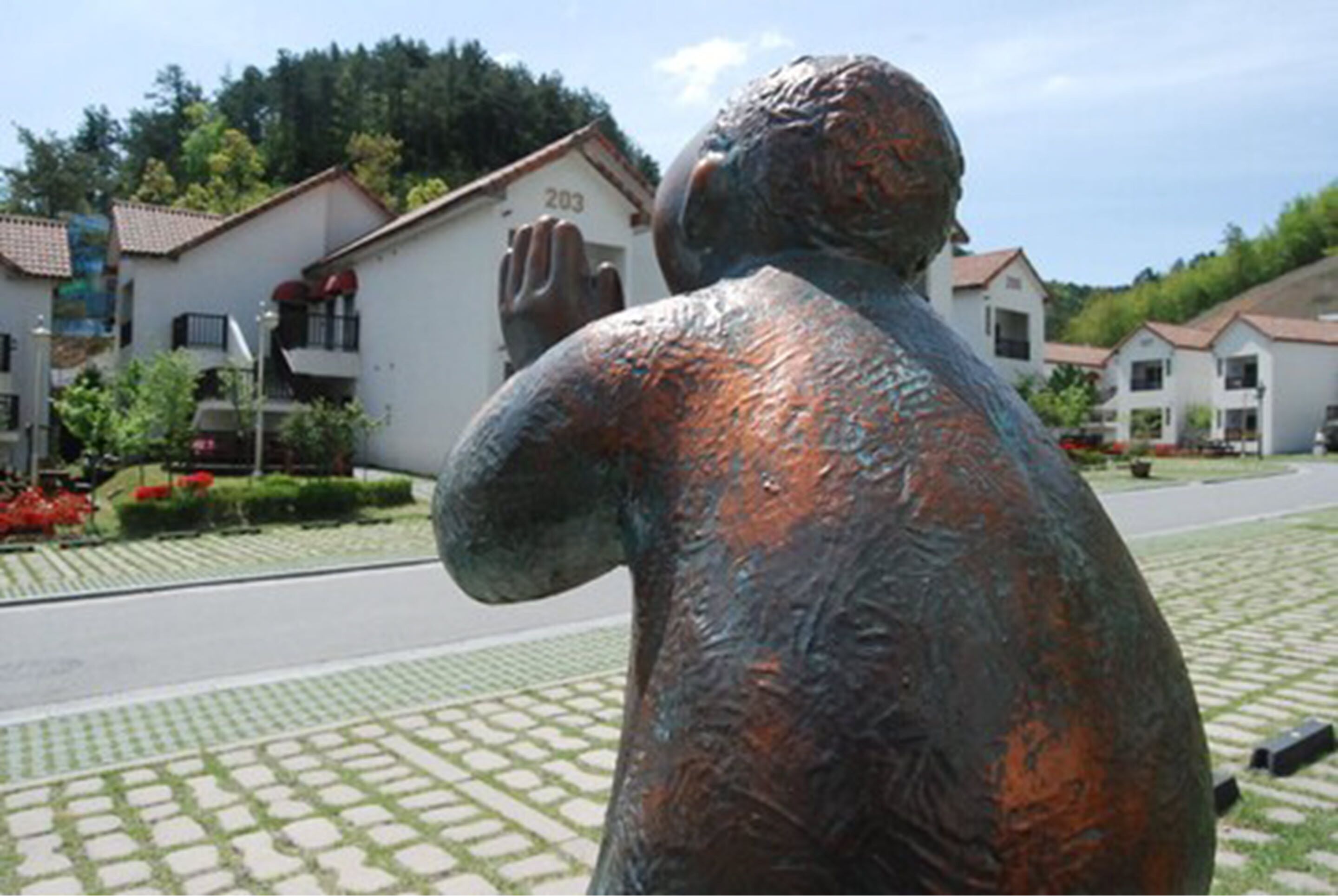 A bronze statue of a person with outstretched arms, located in a paved area with buildings in the background.