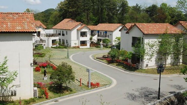 Ein Wohngebiet mit weißen Häusern, einer gewundenen Straße und viel Grün.