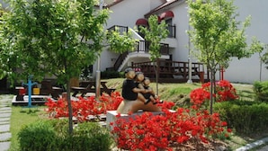 Ein Innenhof mit einer Statue von zwei Figuren, einem Gebäude mit einem Balkon und roten blühenden Pflanzen.