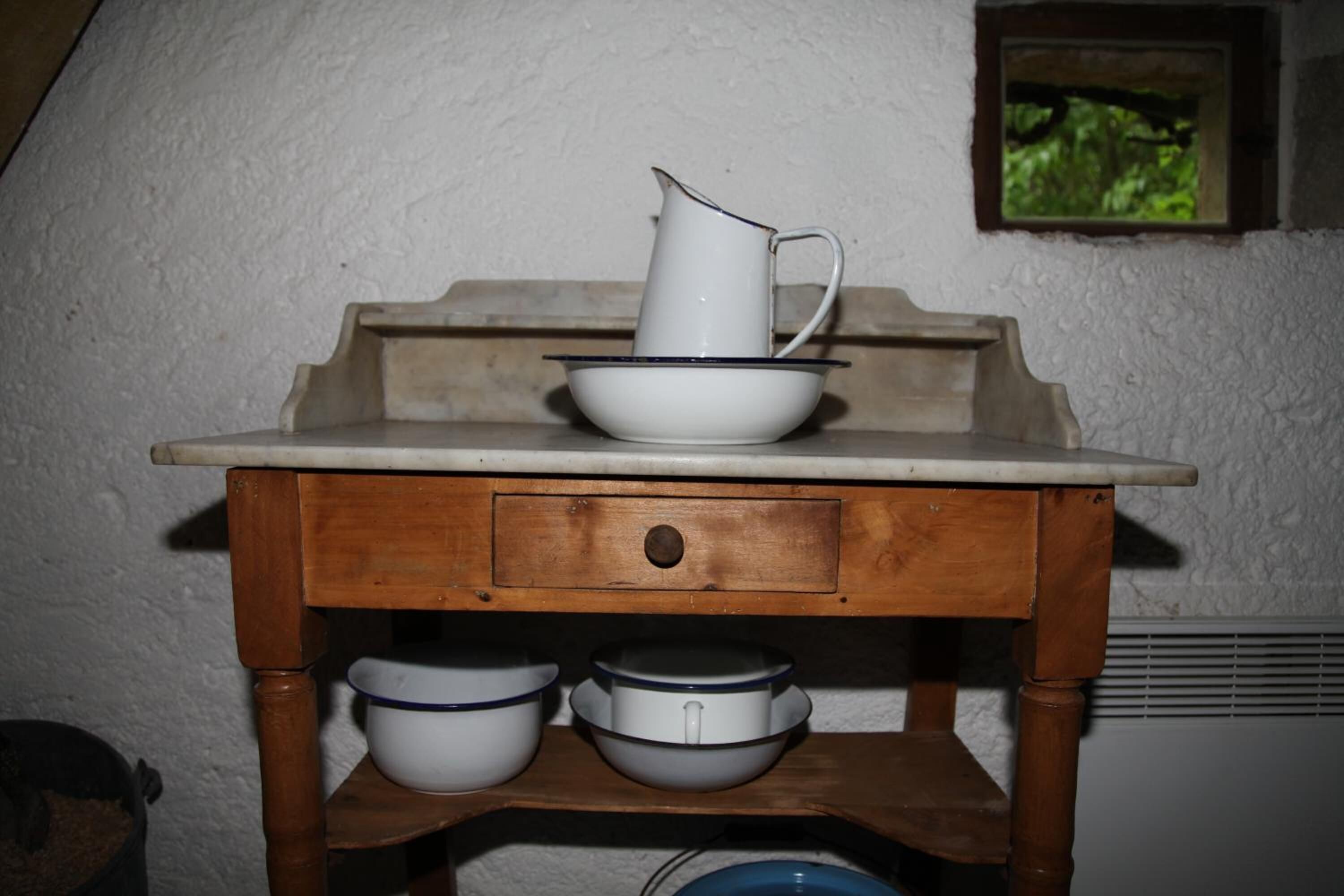 A wooden kitchen counter with a white pitcher, bowls, and a small window with a view of greenery.