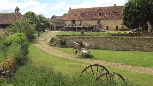 A rural village with stone walls, traditional houses, a cart, and a path. - Gîte Le Porteau Enchanteur (Sarzay)