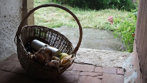 A wicker basket with a bottle and a yellow object on a brick floor near a doorway. - Gîte Le Porteau Enchanteur (Sarzay)