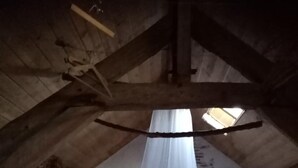 A rustic attic bedroom with a high ceiling, exposed wooden beams, a bed with a white canopy, and a skylight. - Gîte Le Porteau Enchanteur (Sarzay)