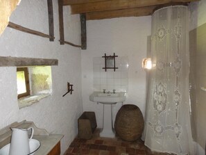 A rustic bathroom with a white sink, a wooden bucket, and a woven basket. - Gîte Le Porteau Enchanteur (Sarzay)