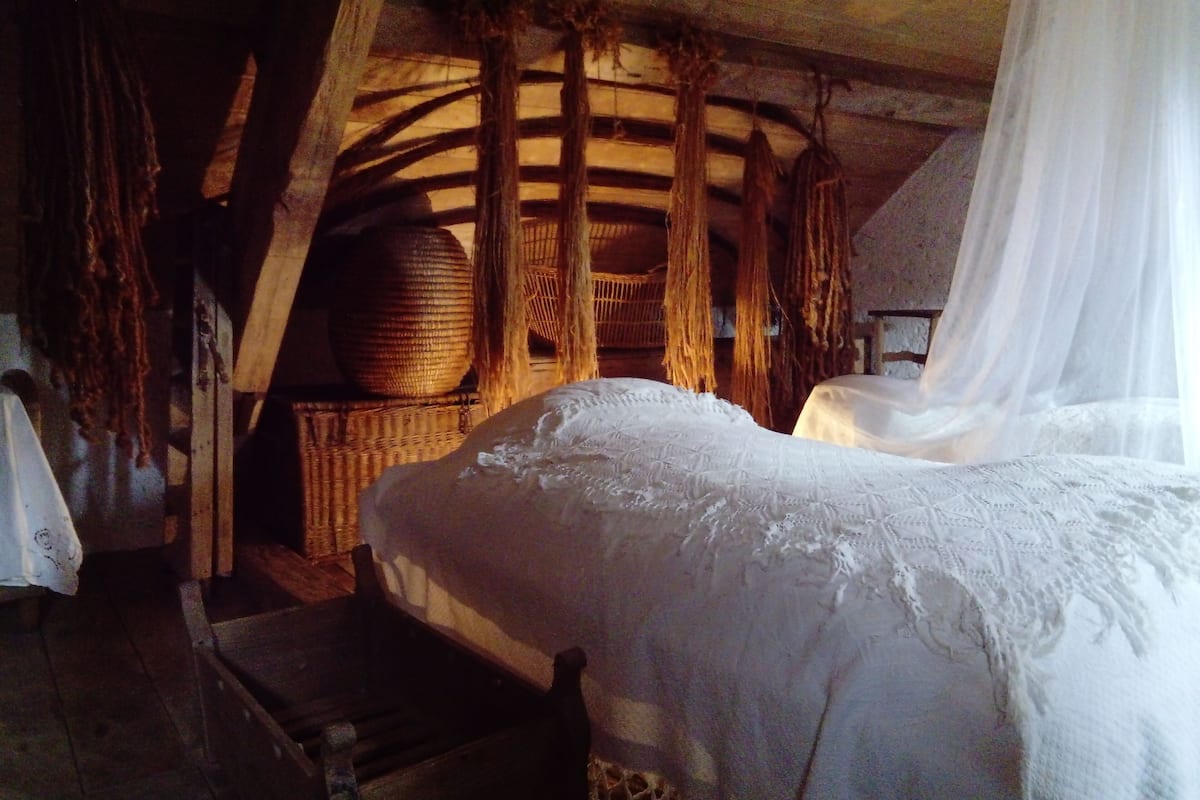 A rustic room with a bed, wooden beams, a woven basket, and a canopy.