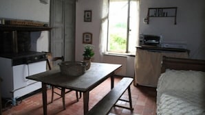 A rustic kitchen with a wooden table, bench, and a window with a view of greenery. - Gîte Le Porteau Enchanteur (Sarzay)