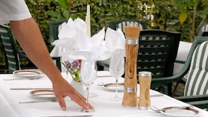 A table set for dining outdoors with white tablecloths, silverware, and a centerpiece of white flowers. - Hotel Sterkel (Roedermark)