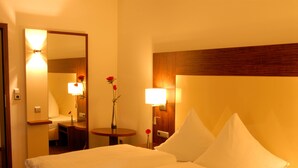 A hotel room with a large bed, a bedside table, a mirror, and a small table with a vase of flowers. - Hotel Sterkel (Roedermark)
