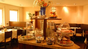 A buffet setup with various food items, a vase with flowers, and a seating area with tables and chairs. - Hotel Sterkel (Roedermark)