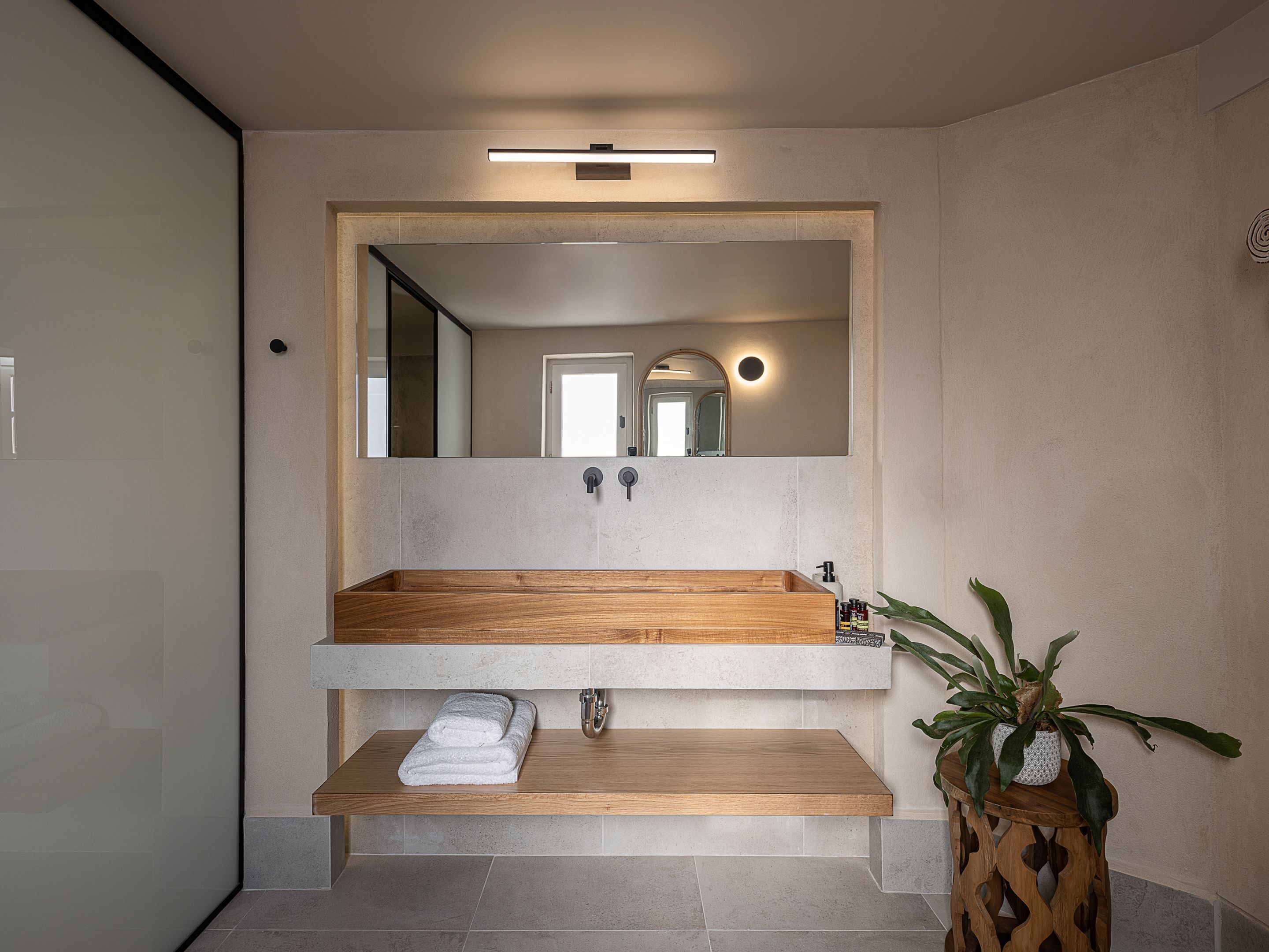 A modern bathroom with a wooden vanity, a large mirror, and a potted plant.