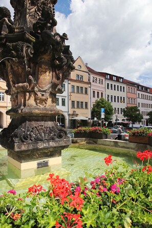 A fountain with intricate carvings and a plaque, surrounded by vibrant flowers. - Hotel Zittauer Hof (Zittau)